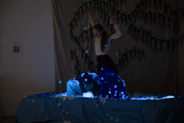 A photo of the dancers, bathed in blue light, interacting an inflatable pool full of flower petals during the performance.